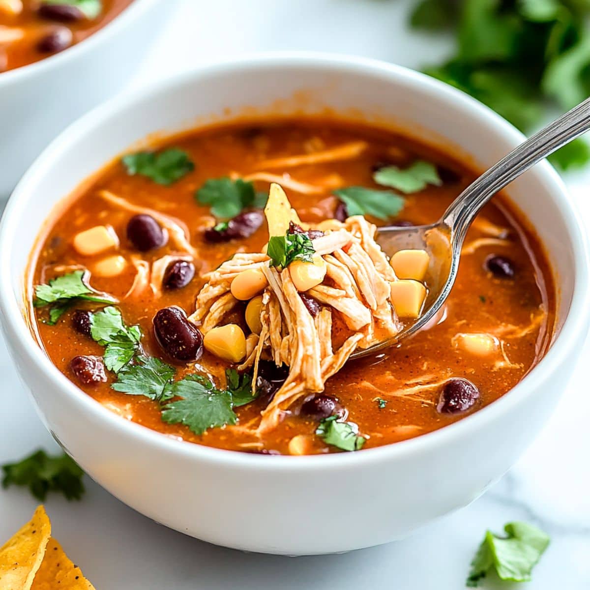 Spoon lifting a scoop of chicken enchilada soup in a white bowl.