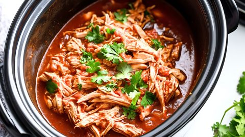 Shredded chicken cooked inside a slow cooker with tomato sauce.