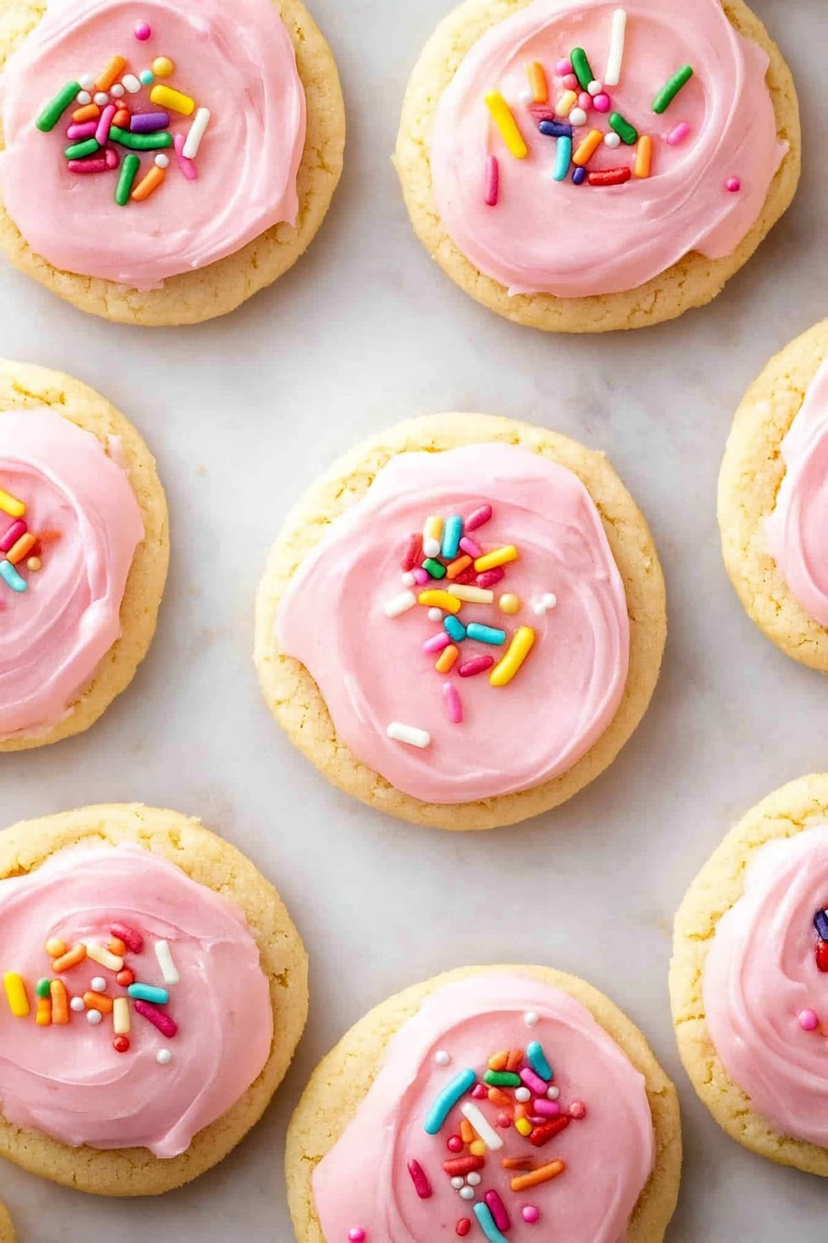 Soft frosted sugar cookies with pink frosting and candy sprinkles, top view.