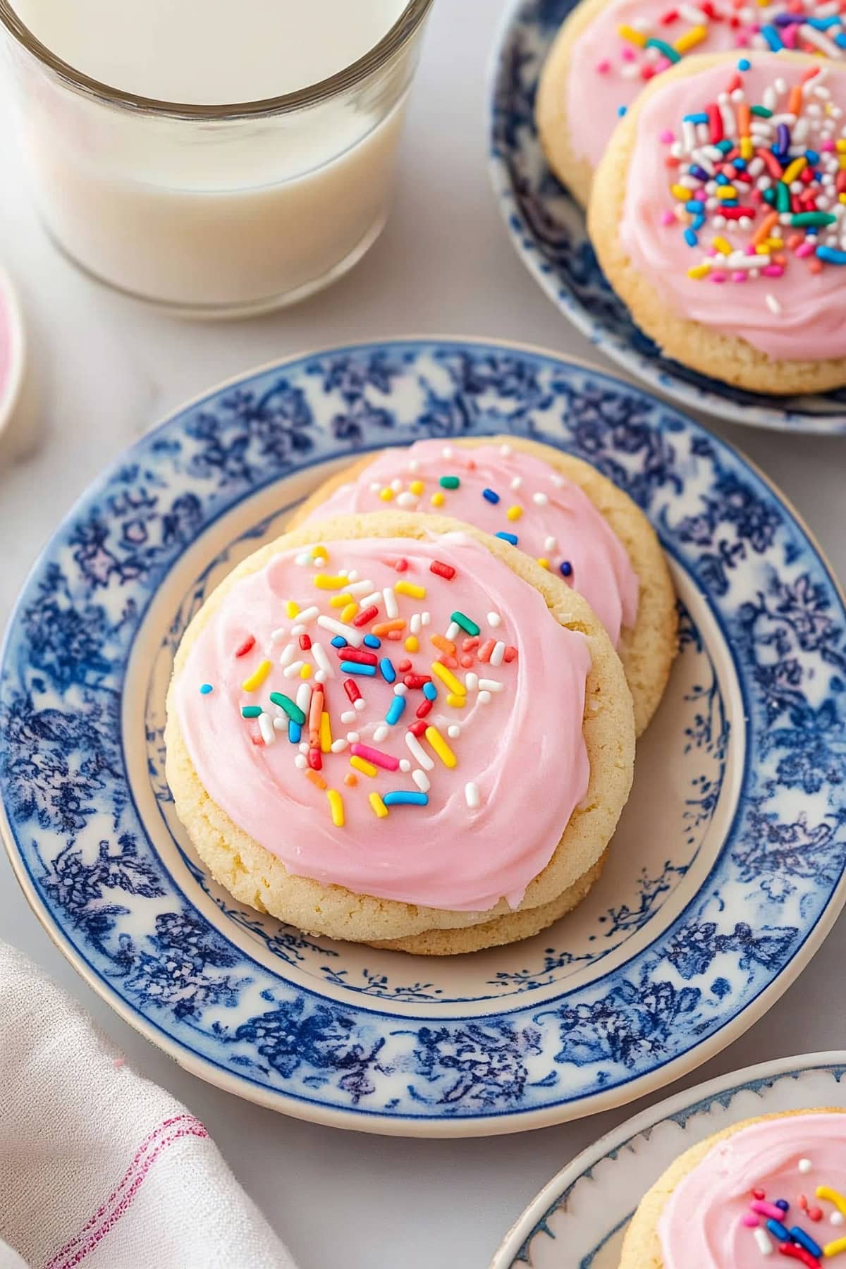 Soft frosted sugar cookies stacked on a plate, served with milk, top view