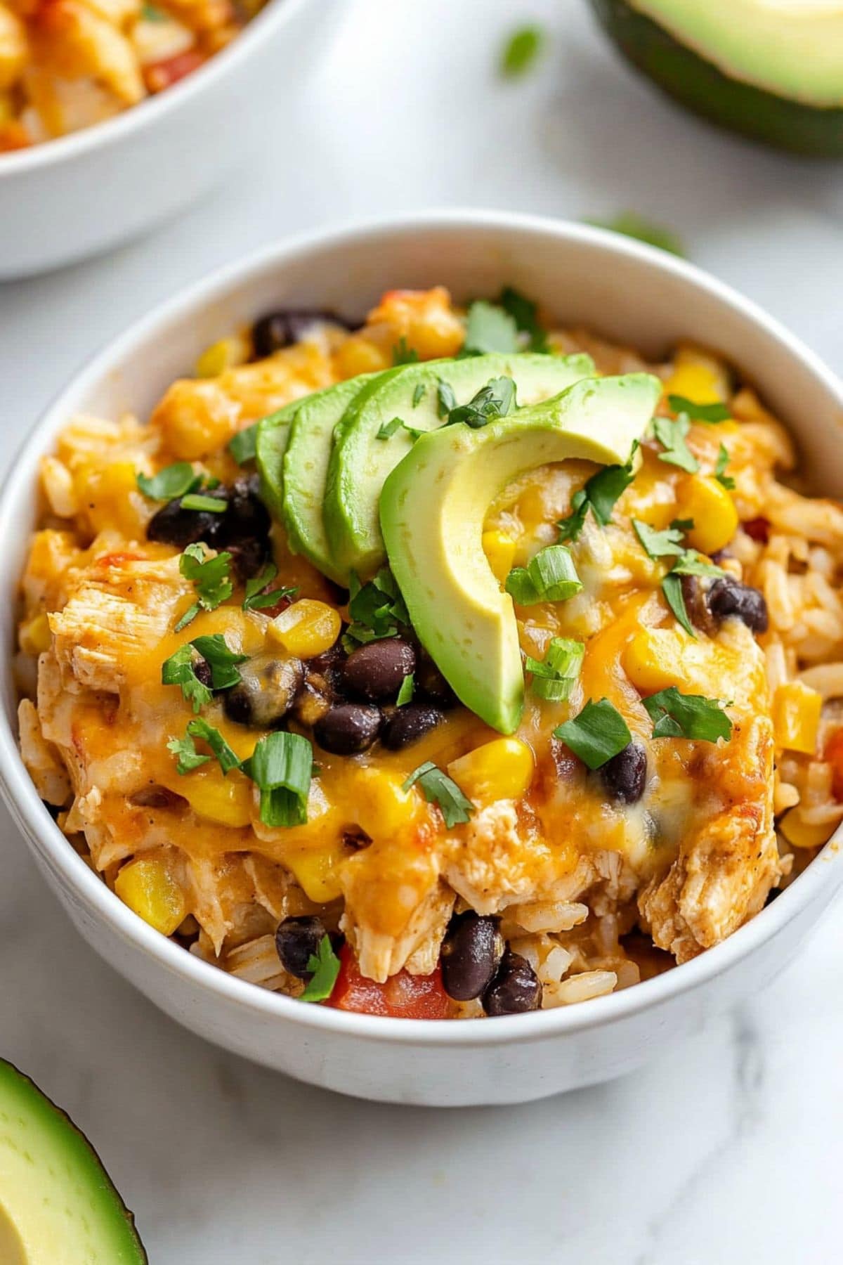 Chicken casserole served in a white bowl topped with slices of avocado.