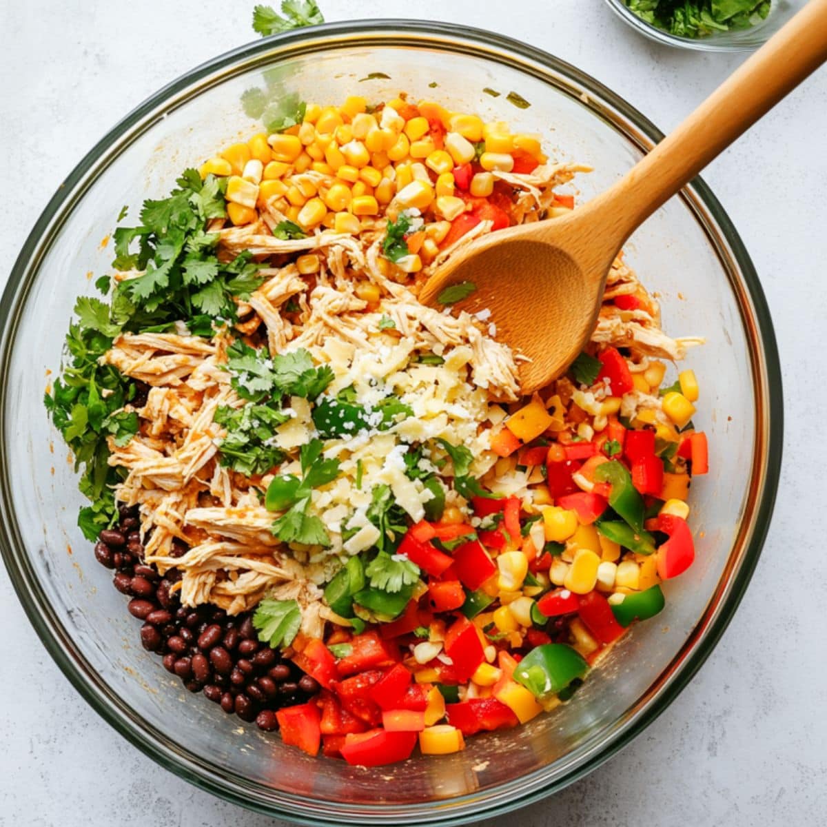 Shredded chicken, black beans, corn, bell pepper, onion, jalapeno, cilantro, pepper jack cheese, chili powder, cumin, garlic powder, smoked paprika, salt, and pepper mixed in a large glass mixing bowl. 