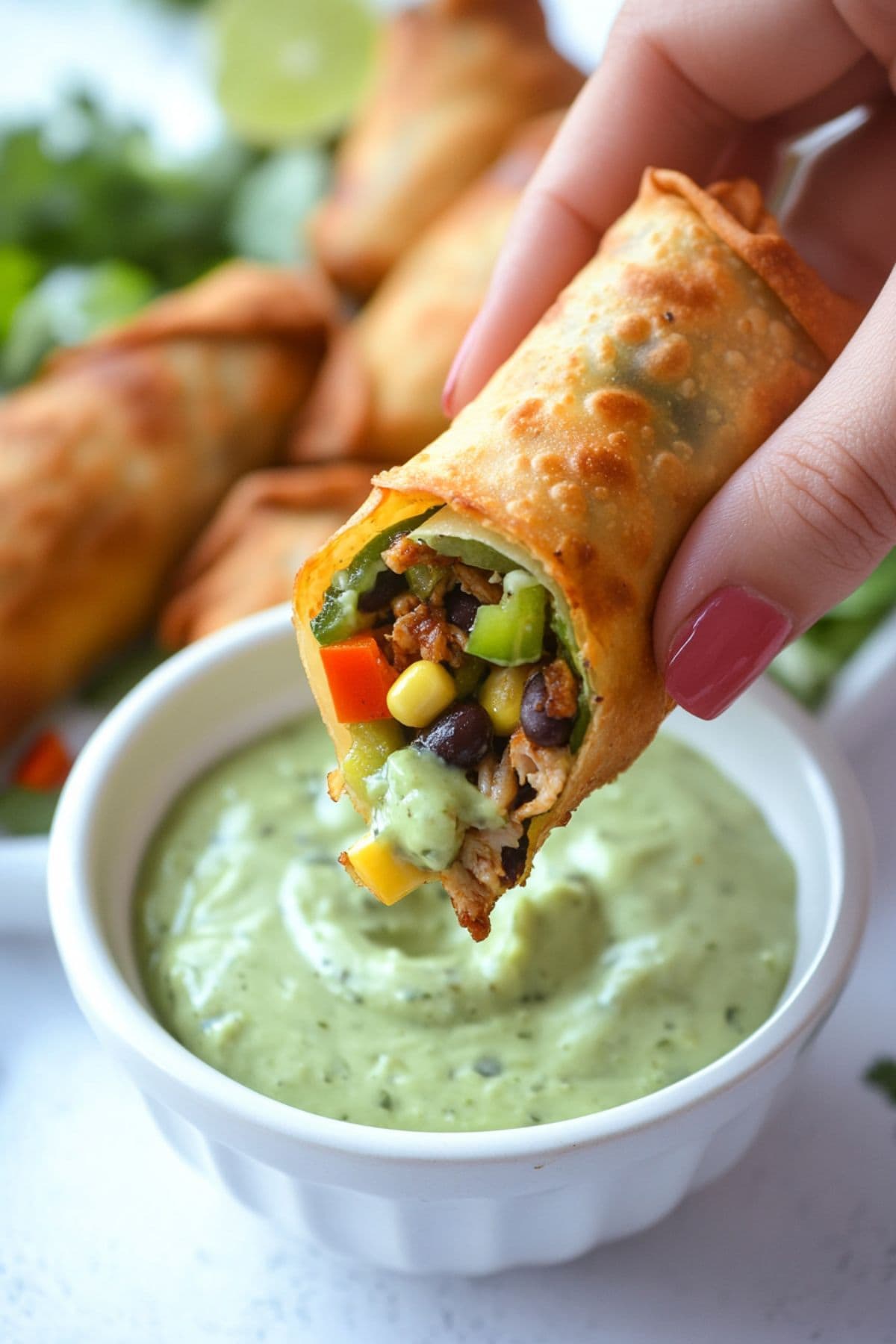 Egg roll with chicken, colorful veggies, and melty cheese filling dipped into avocado dressing.