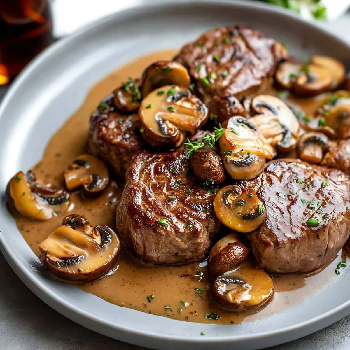 A close-up shot of steak Diane with mushrooms and herbs on a plate.