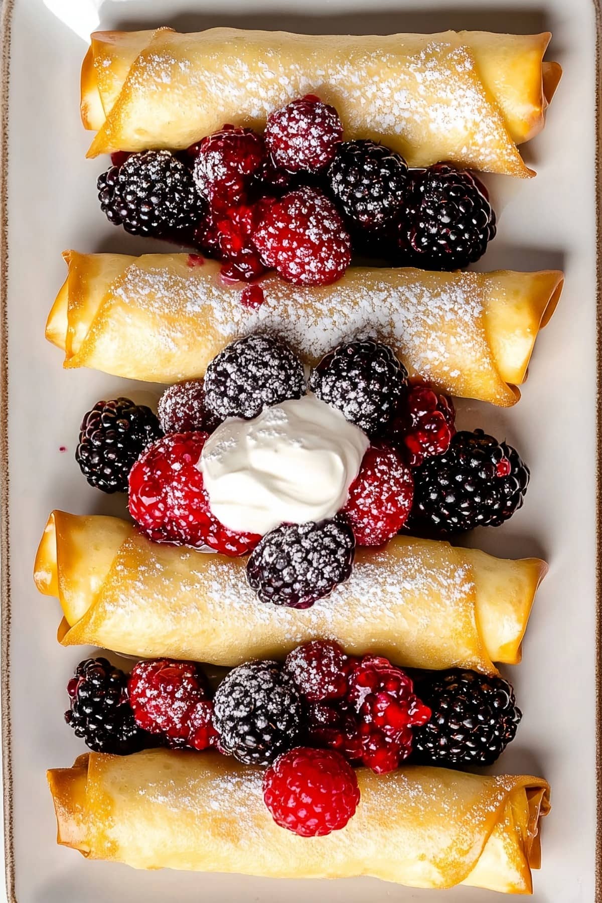 Overhead shot of cheese blintzes with a side of mixed berries and whipped cream.