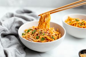 Wooden chopsticks holding a sweet and spicy noodles in a bowl.