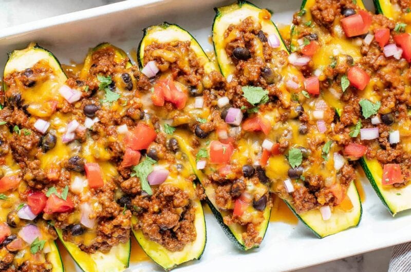 An overhead view of cheesy taco zucchini boats with ground beef and black beans in a white baking dish.