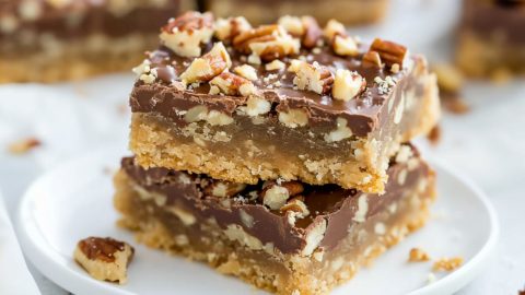 Toffee bars square slices topped with chopped pecans served on a white plate.