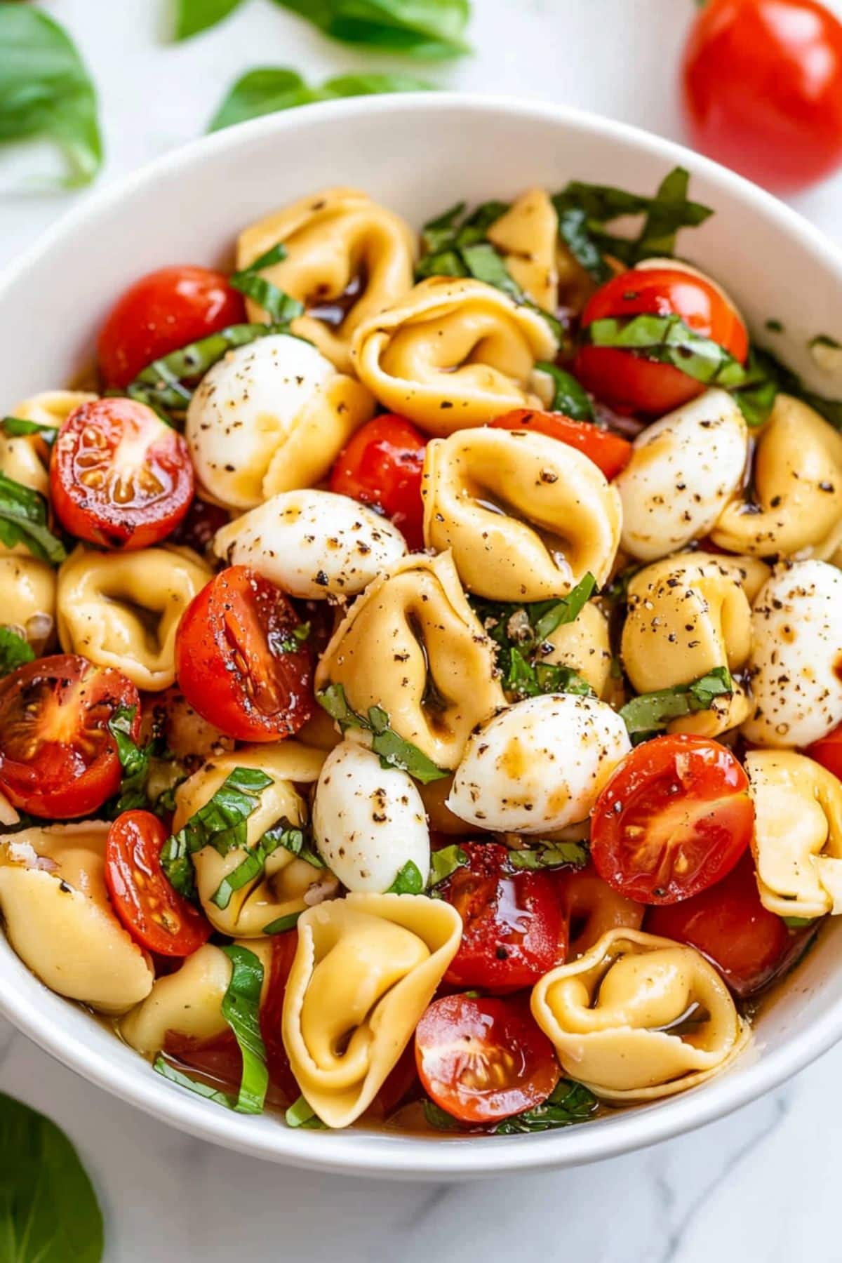 Serving of tortellini caprese salad in a white bowl.