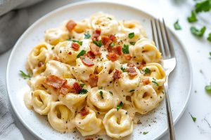 Tortellini carbonara on a white plate garnished with bacon bits.