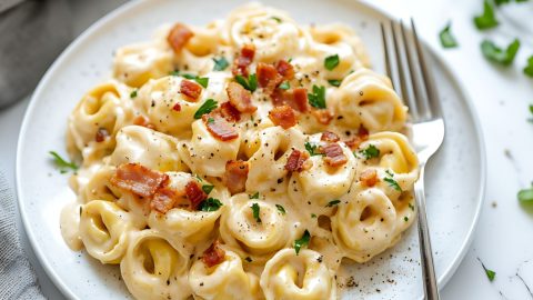 Tortellini carbonara on a white plate garnished with bacon bits.