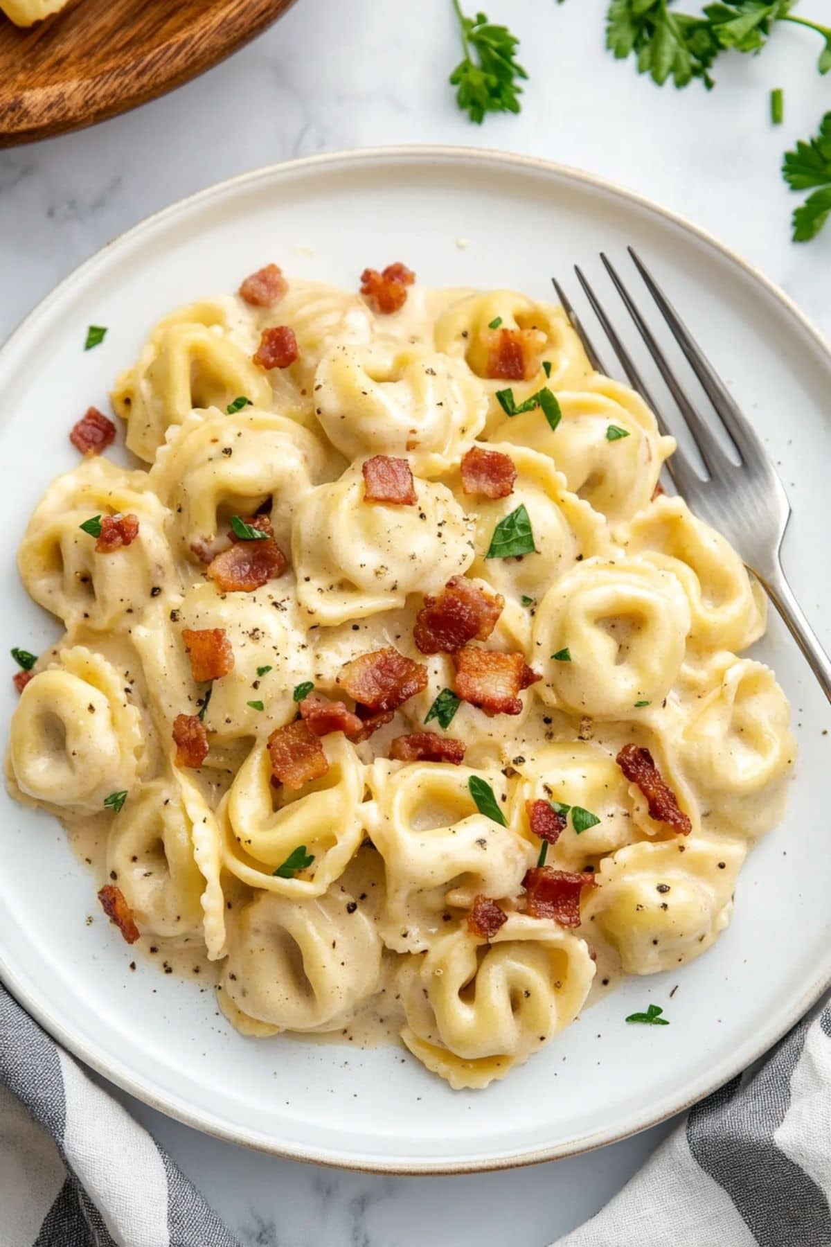 Serving of creamy tortellini pasta in a white plate, fork ion the side. 