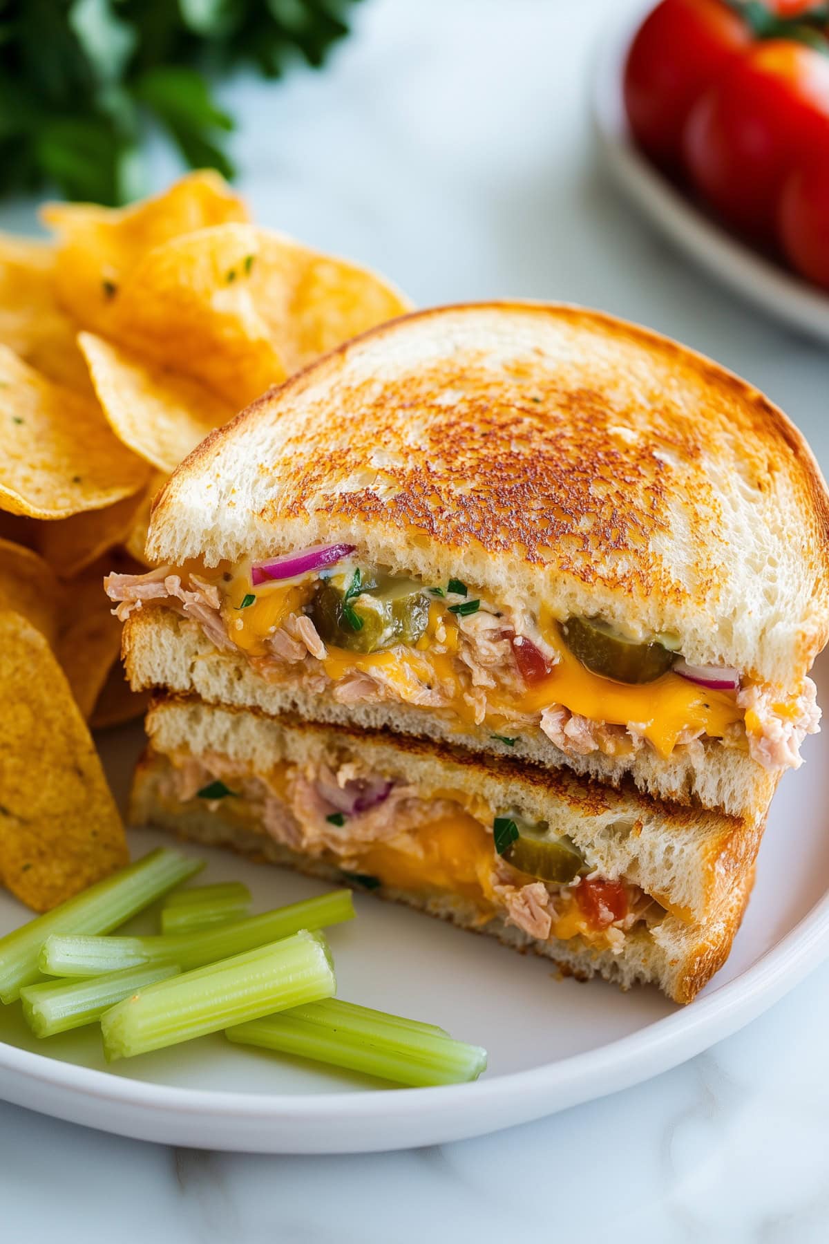 Tuna melt oozing with cheese, served hot on a plate with a side of chips and celery.