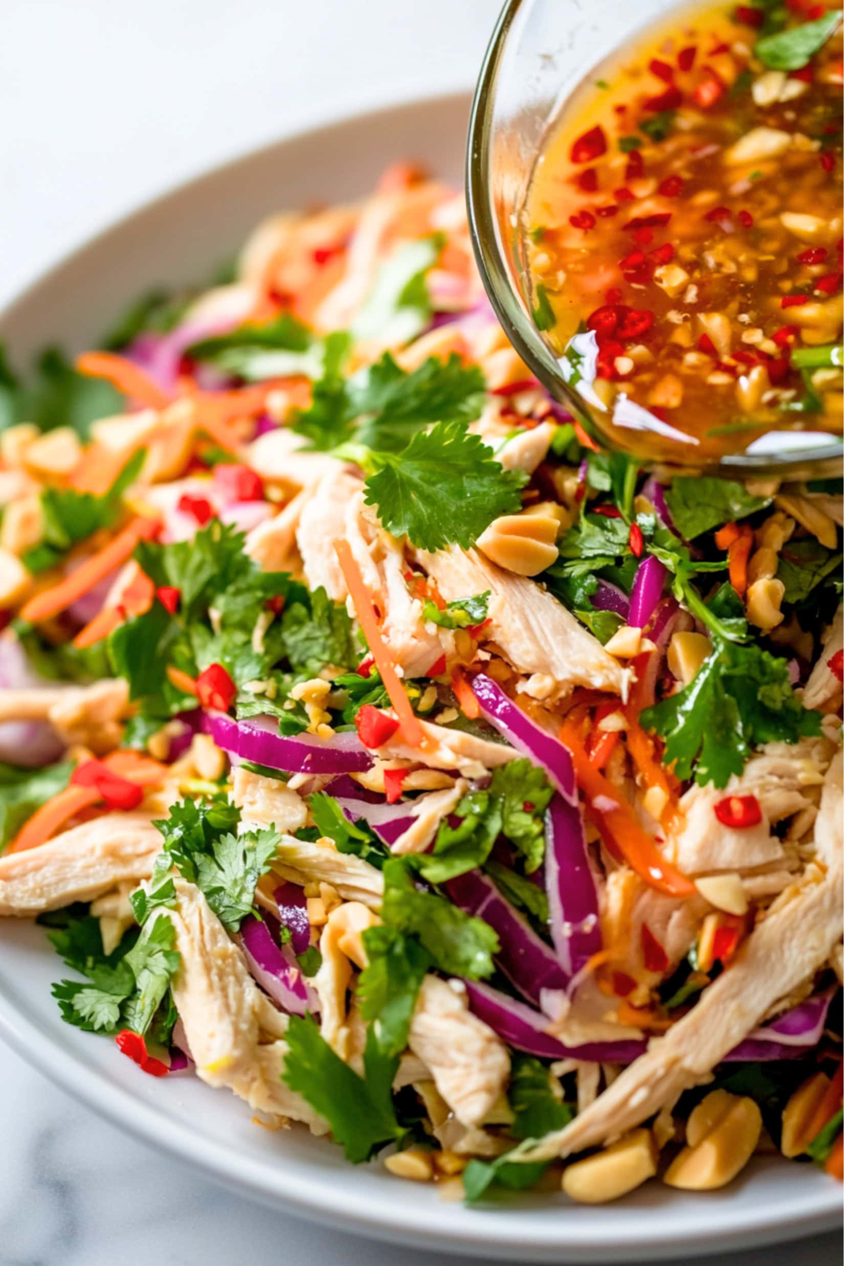 Nuoc Cham dressing poured to  shredded cabbage, carrots, onions, cilantro leaves and chopped peanuts served on a white plate.
