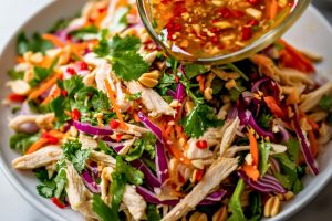 Dressing poured over Vietnamese chicken salad in a white plate.