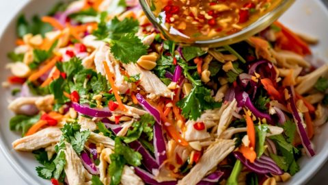 Dressing poured over Vietnamese chicken salad in a white plate.