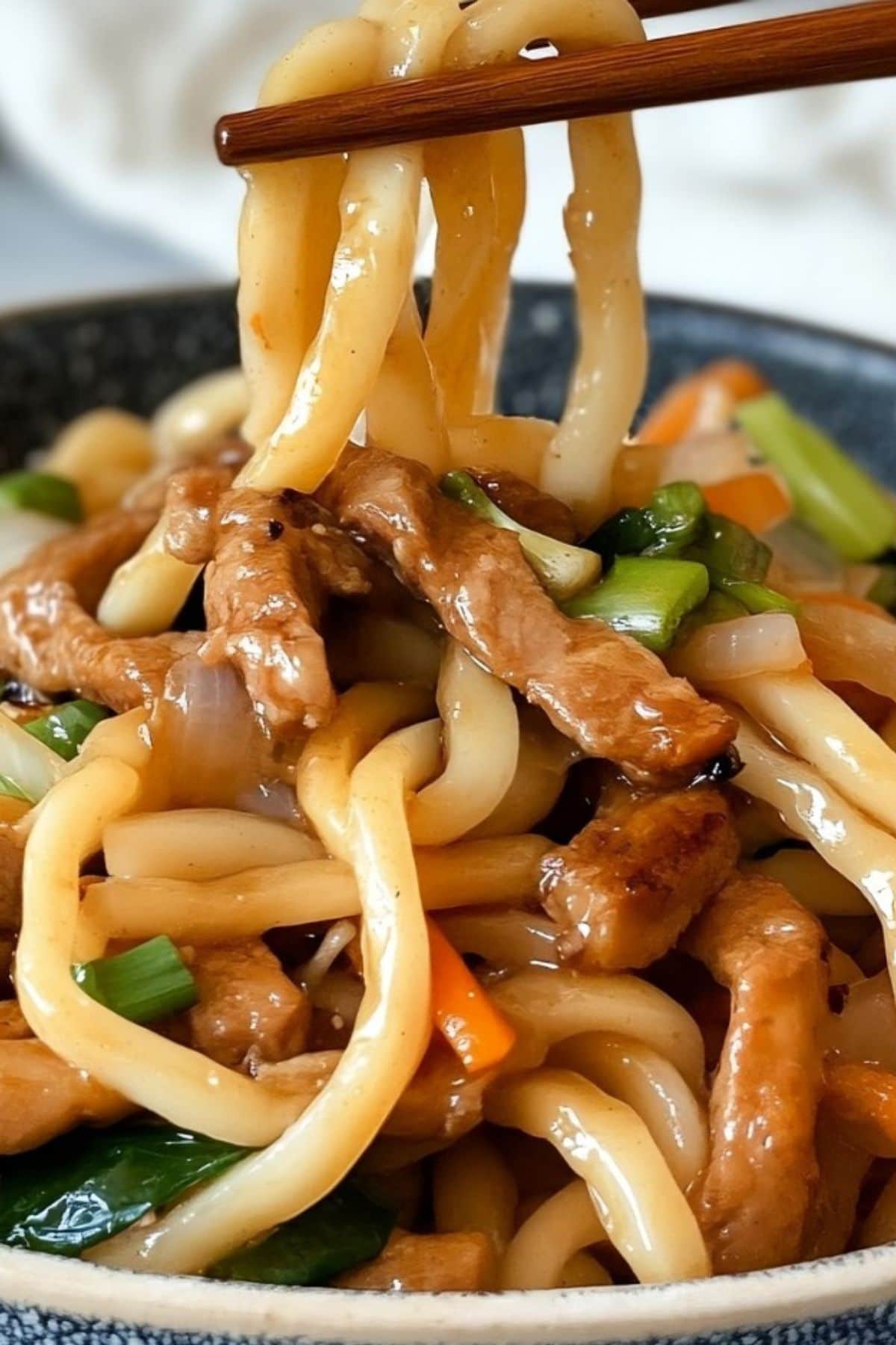 Chopsticks picking yaki udon from a bowl.