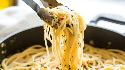 Spaghetti aglio o olio in a pan lifted with a tong.
