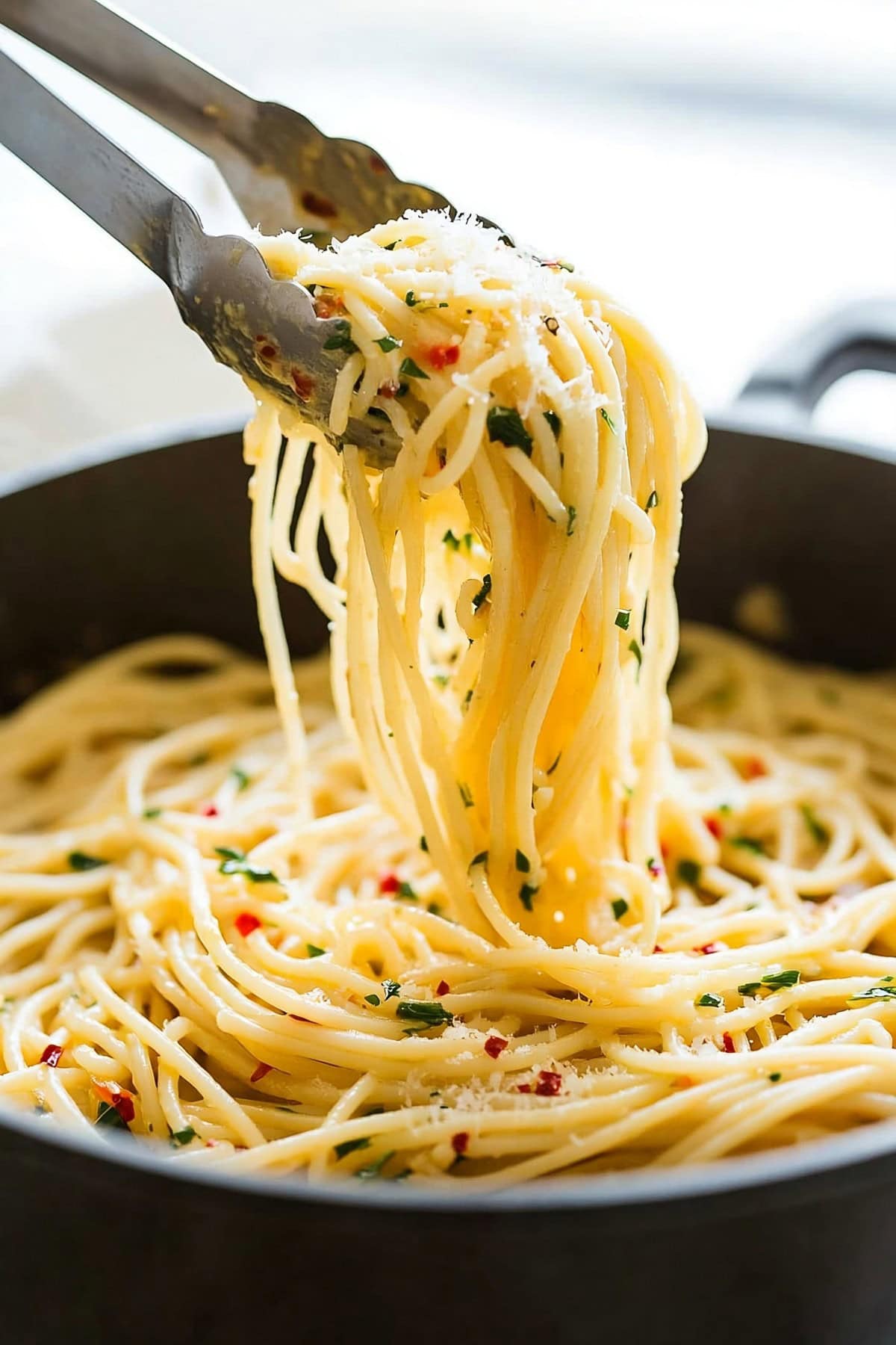 Tong lifting spaghetti aglio e alio with parmesan cheese  from pan. 