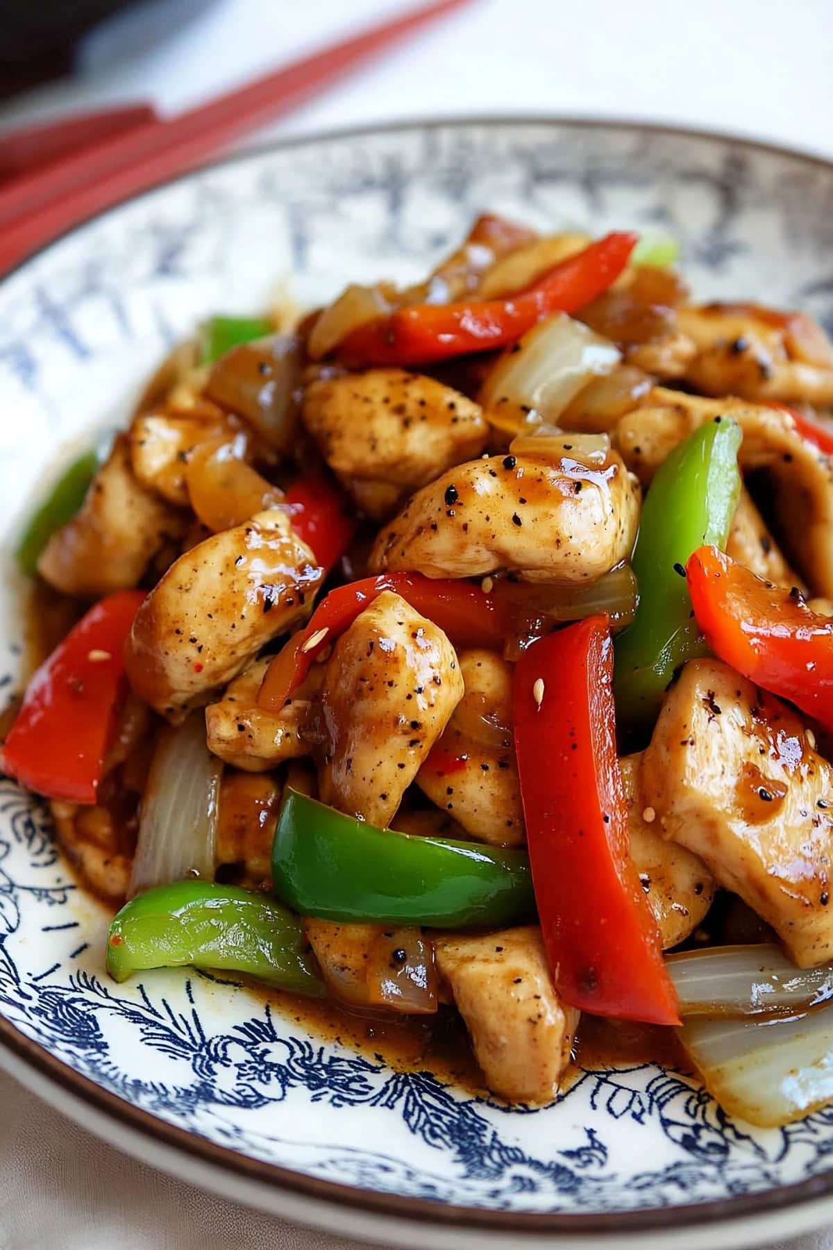 Chicken chunks with red and green bell peppers coated in black pepper sauce served on a white plate.