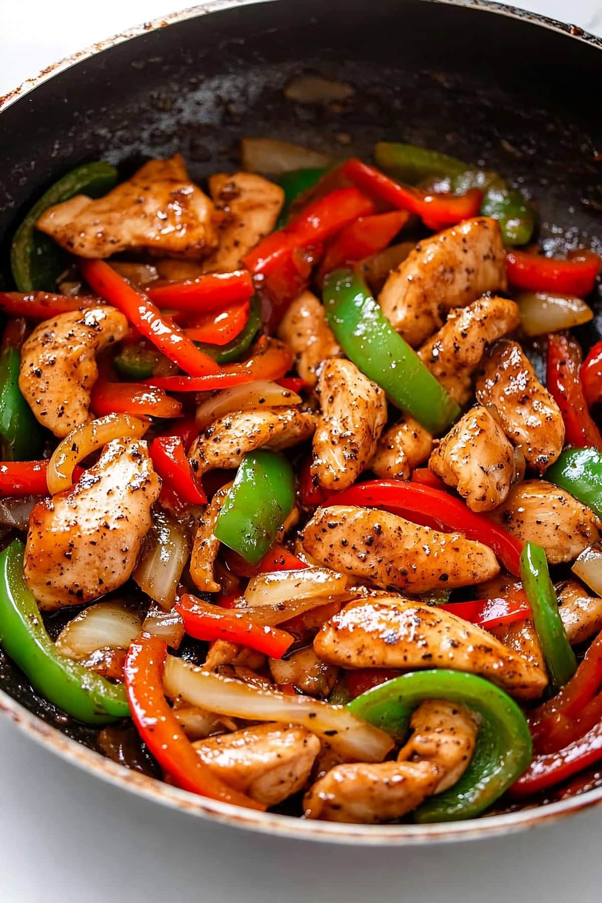 Tender chunks of chicken coated in black pepper sauce with colorful bell peppers and onions cooked in a skillet pan.