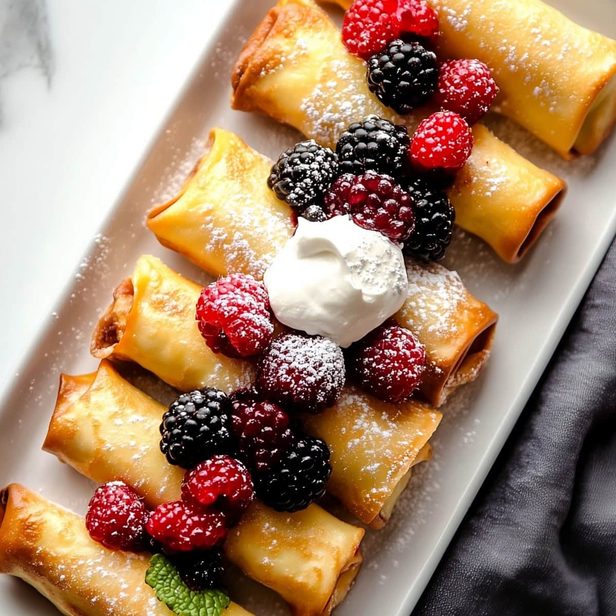 A plate of cheese blintzes with berries and sprinkled with powdered sugar.