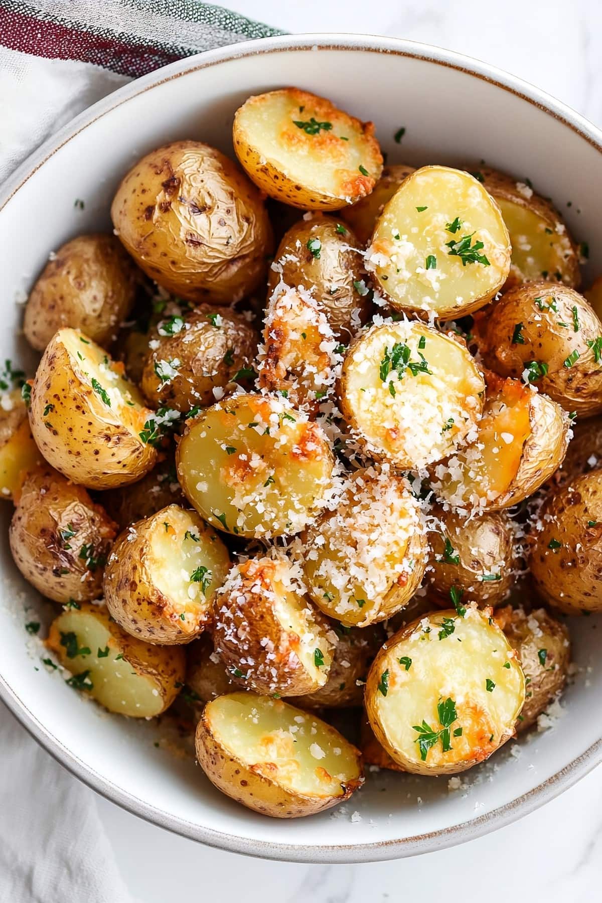 White bowl with crispy potatoes sliced in half baked with butter and garlic.