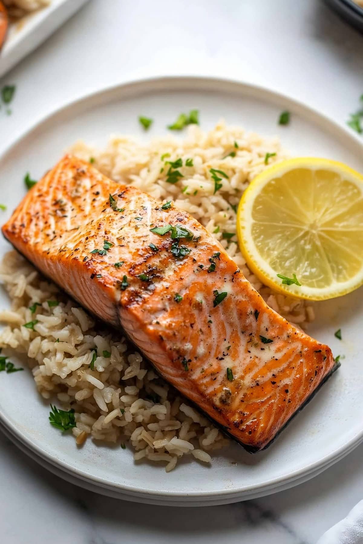 Garlic butter salmon served on top of rice garnished with lemon slice.