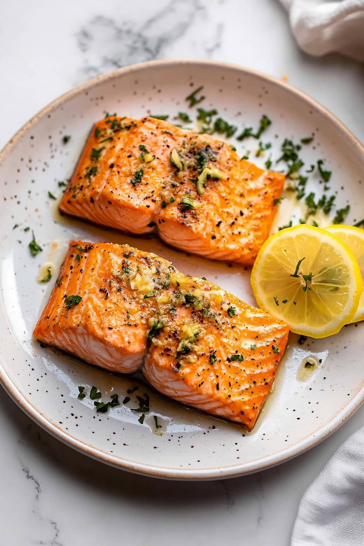 Salmon slices with garlic and butter sauce garnished with lemon wheel served on a plate.