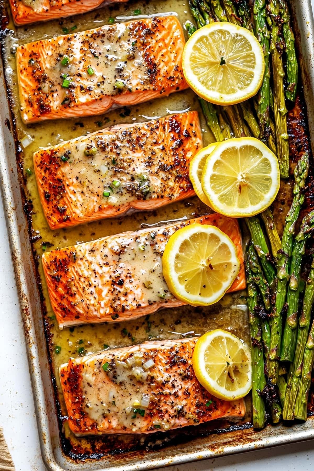 Salmon slices with butter garlic sauce baked in a sheet pan with asparagus and lemon slices.