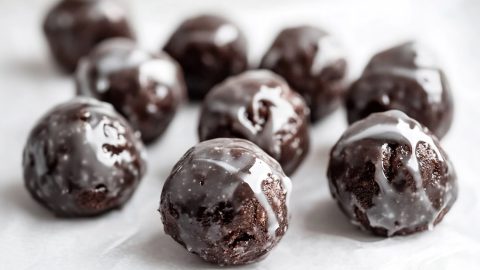 A close-up of glazed chocolate donut holes arranged on parchment paper.
