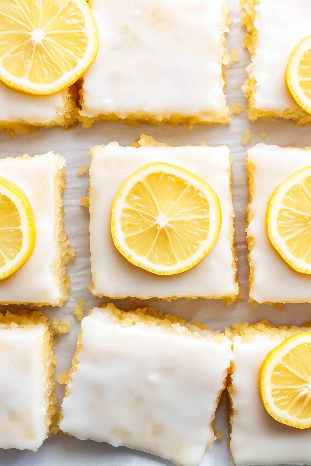 Slices of lemon brownies with lemon glaze on parchment paper.