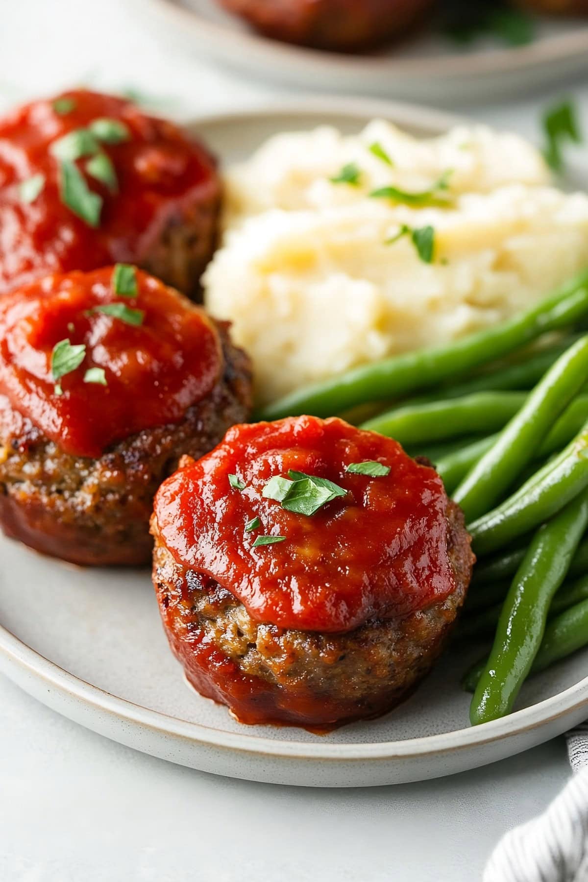 A serving of meatloaf muffins with mashed potatoes and asparagus on the side.