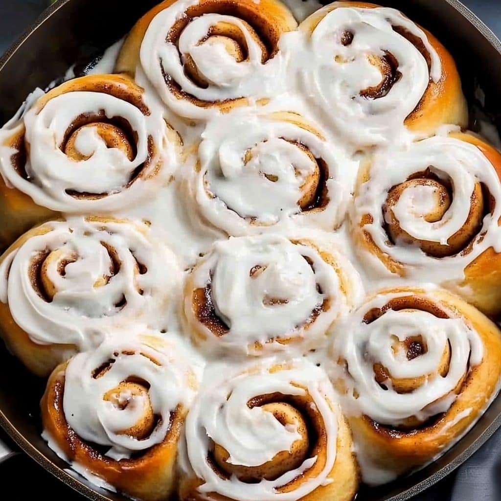 Skillet cinnamon rolls topped with cream cheese icing cooked in a skillet pan.