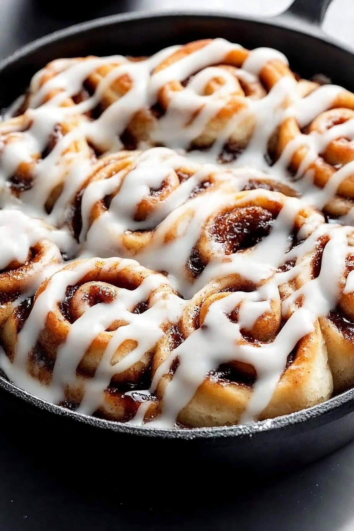 Cinnamon rolls cooked in a skillet drizzled with vanilla cream cheese glaze.