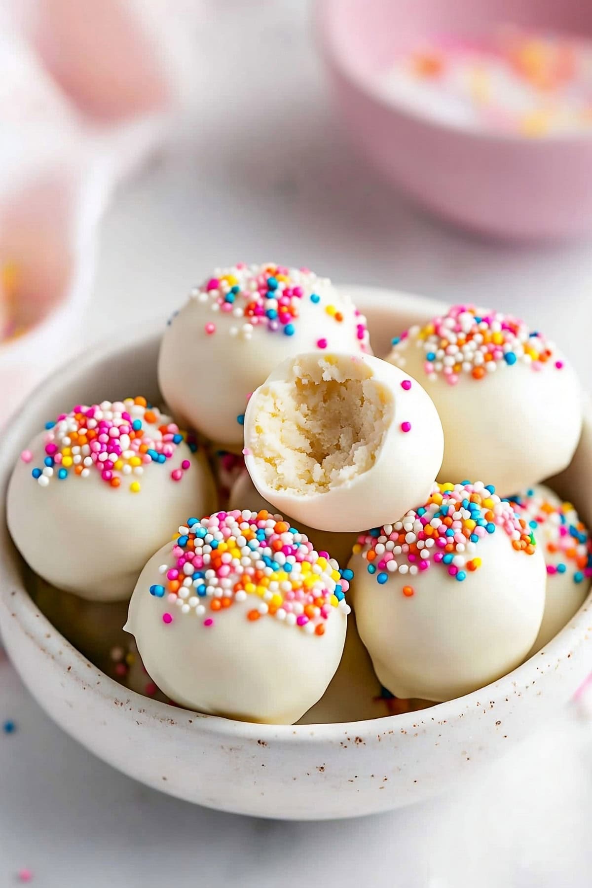 White chocolate coated cookie balls with candy sprinkles arranged in a white bowl.