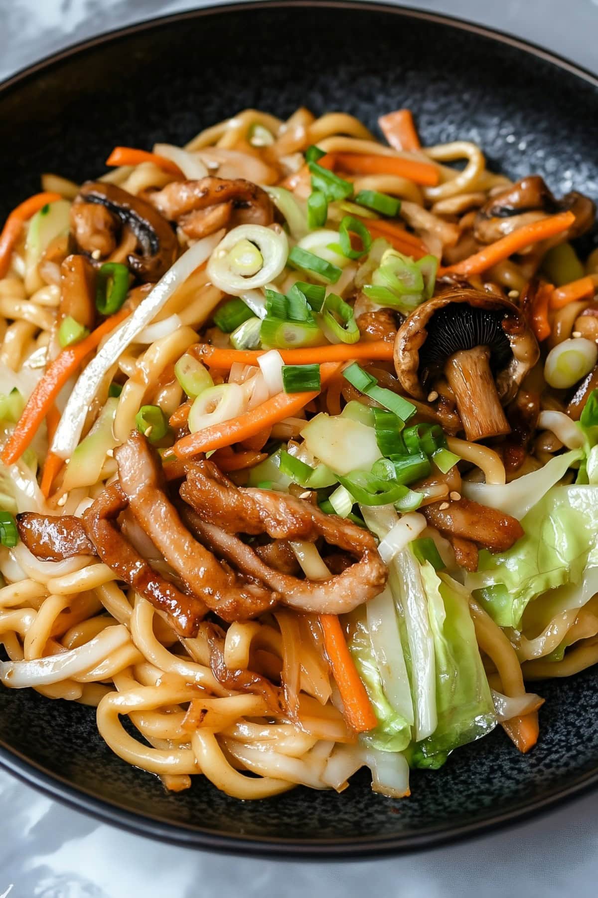 Yaki udon with pork belly, noodles and veggies stir fried in a wok pan.