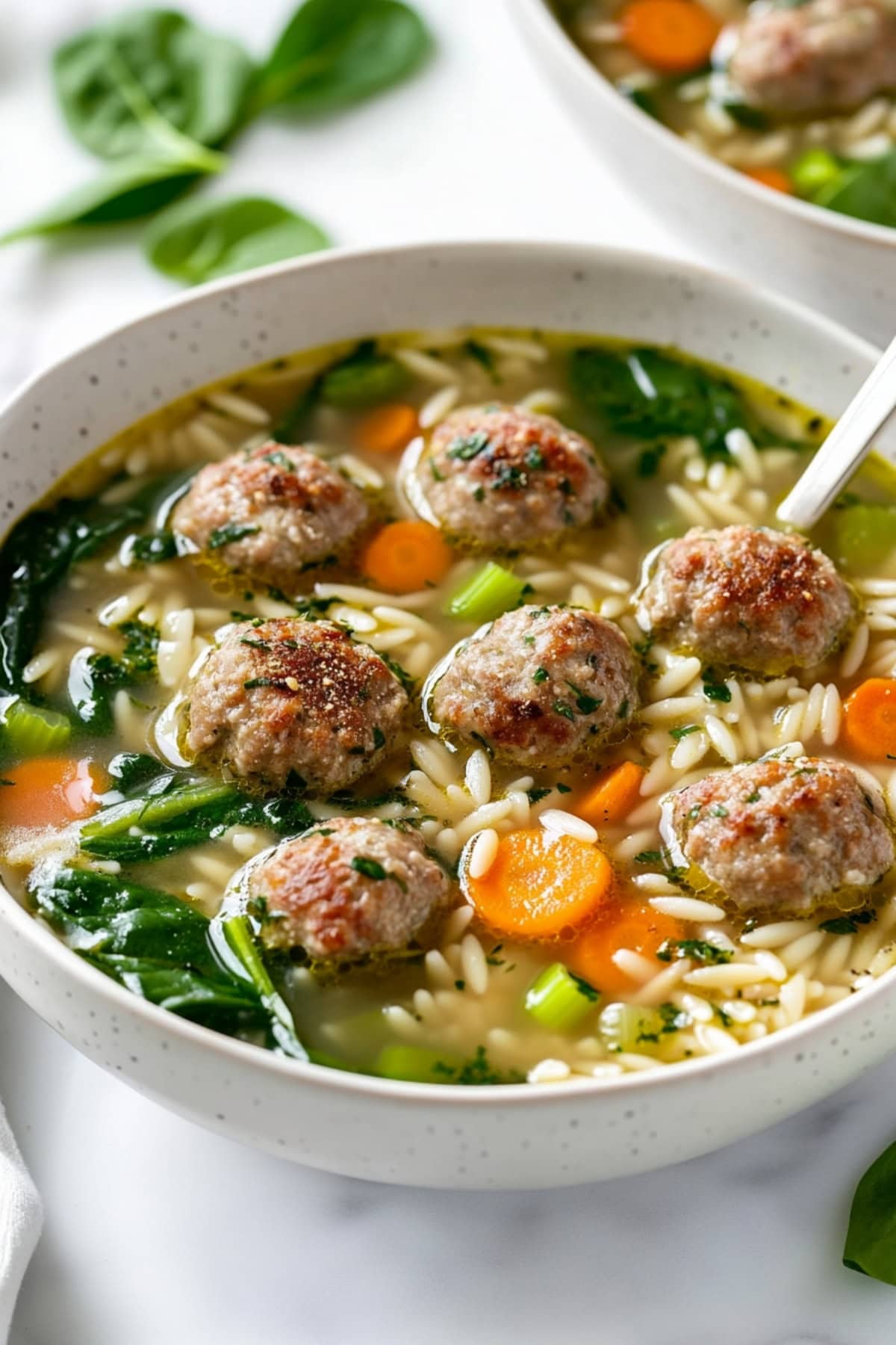 A comforting bowl of Italian wedding soup, showing golden meatballs and fresh vegetables.