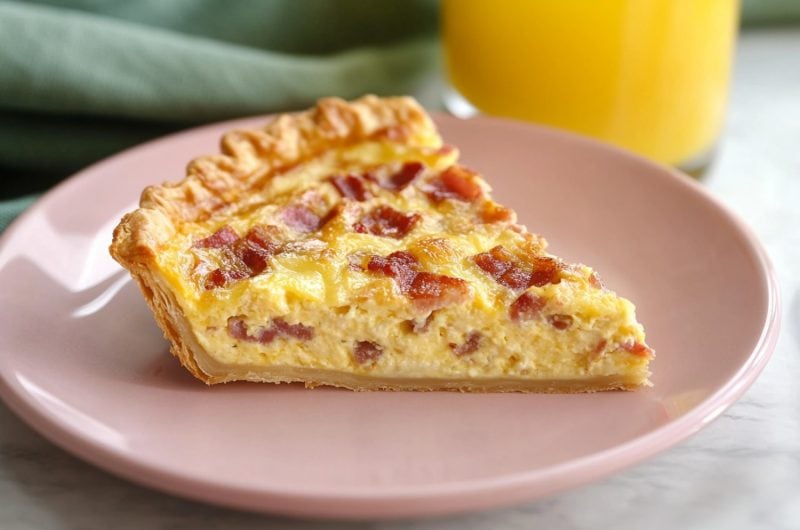 Bacon and cheese quiche cut into a triangular slice, each showing a hearty filling and flaky crust.