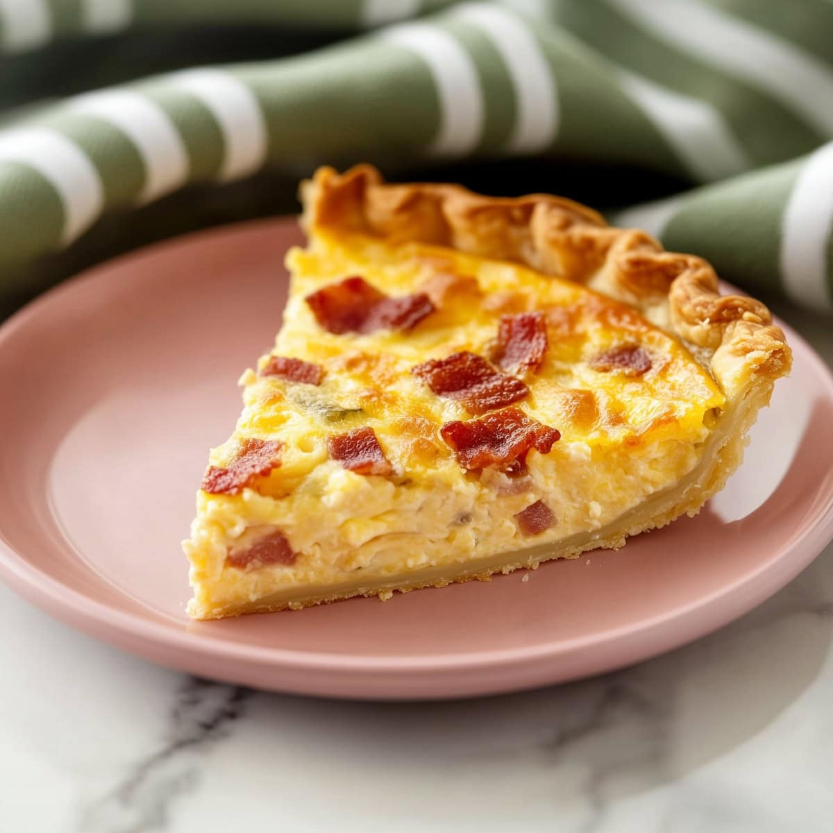 A slice of bacon and cheese quiche served on a pink plate, side view