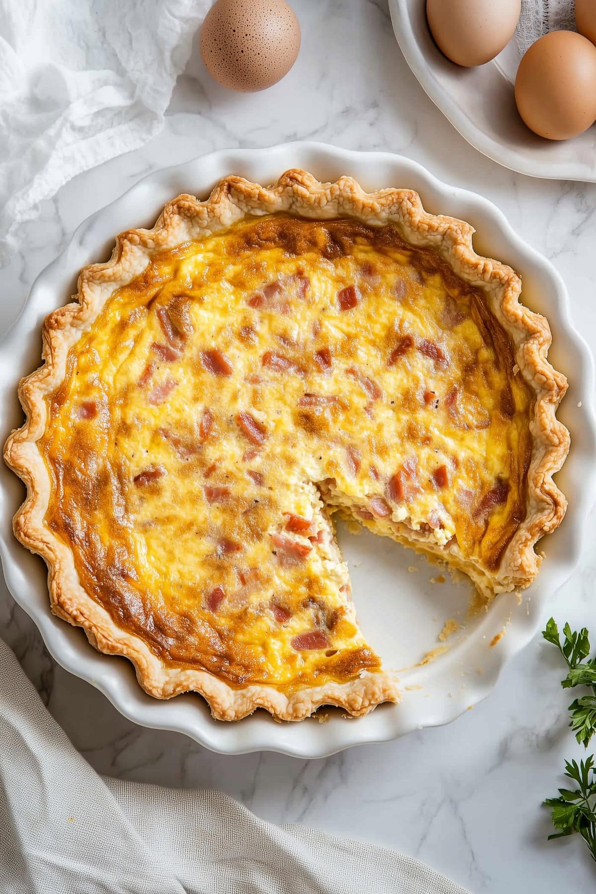 A whole bacon and cheese quiche with a slice removed, in a pie plate, top view