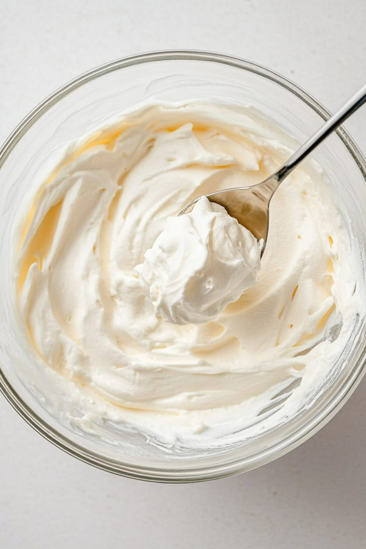 Spoon scooping cold heavy whipping cream in a glass bowl.