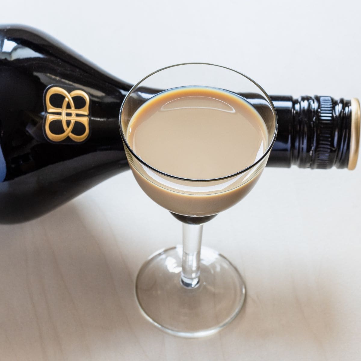 Portion of Irish cream liquor in a wine glass, bottle in the background.