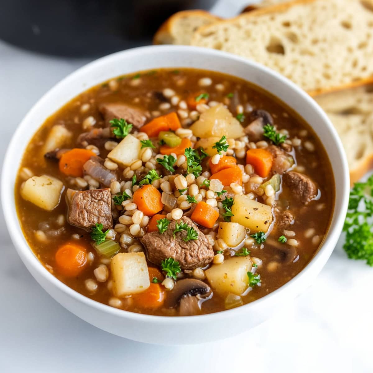 A bowl of beef barley soup with onions, carrots and potatoes.