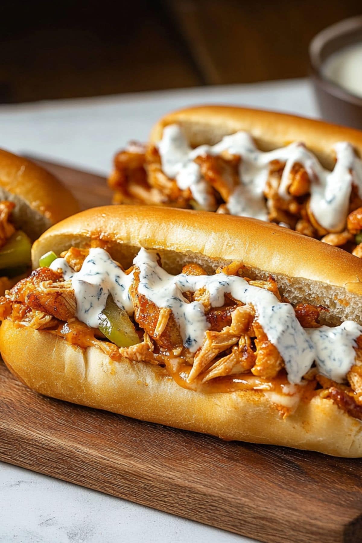 Buffalo chicken cheesesteaks arranged on a wooden board drizzled with blue cheese dressing.