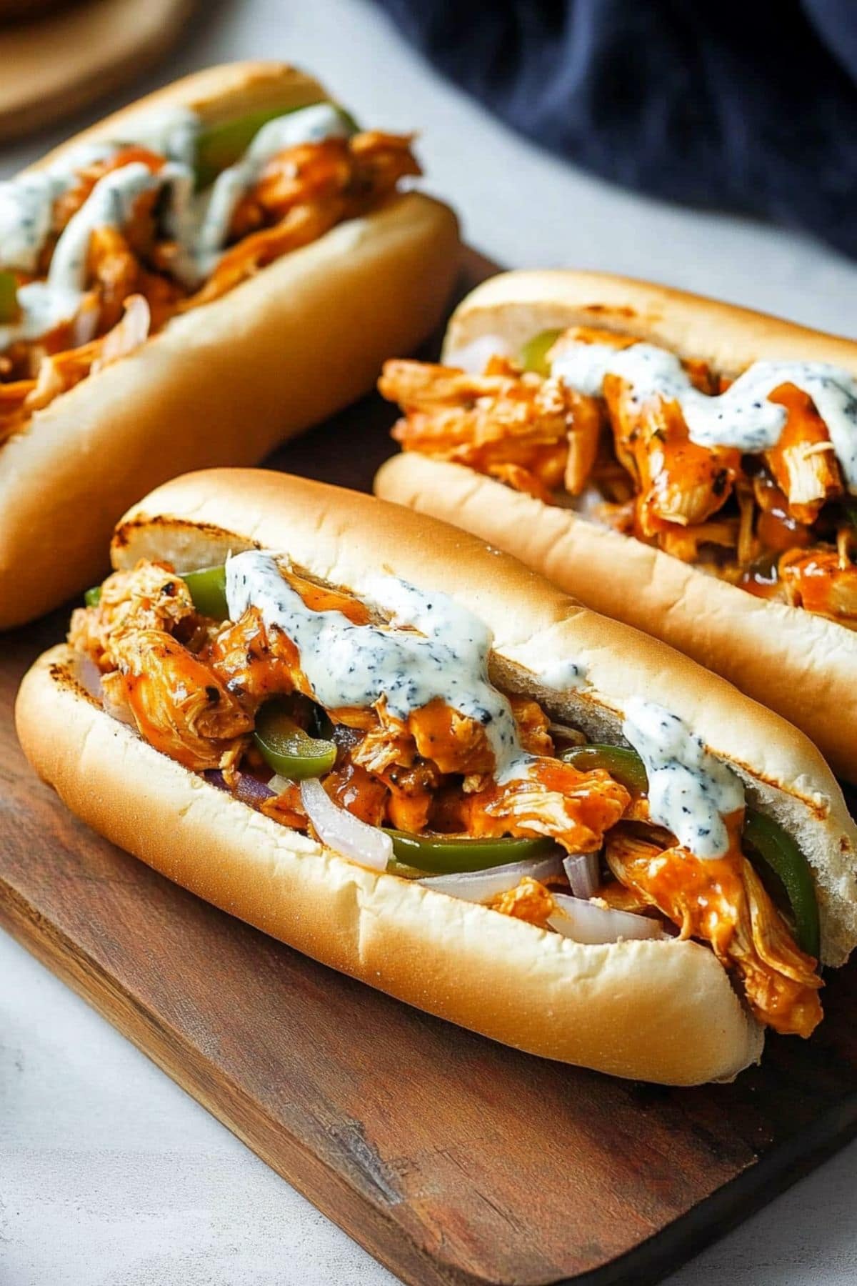 Buffalo Chicken Cheesesteak sandwiches topped with blue cheese dressing on a wooden board.