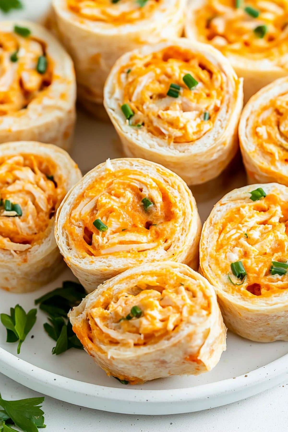 Sliced buffalo chicken pinwheels on a white plate with green onions