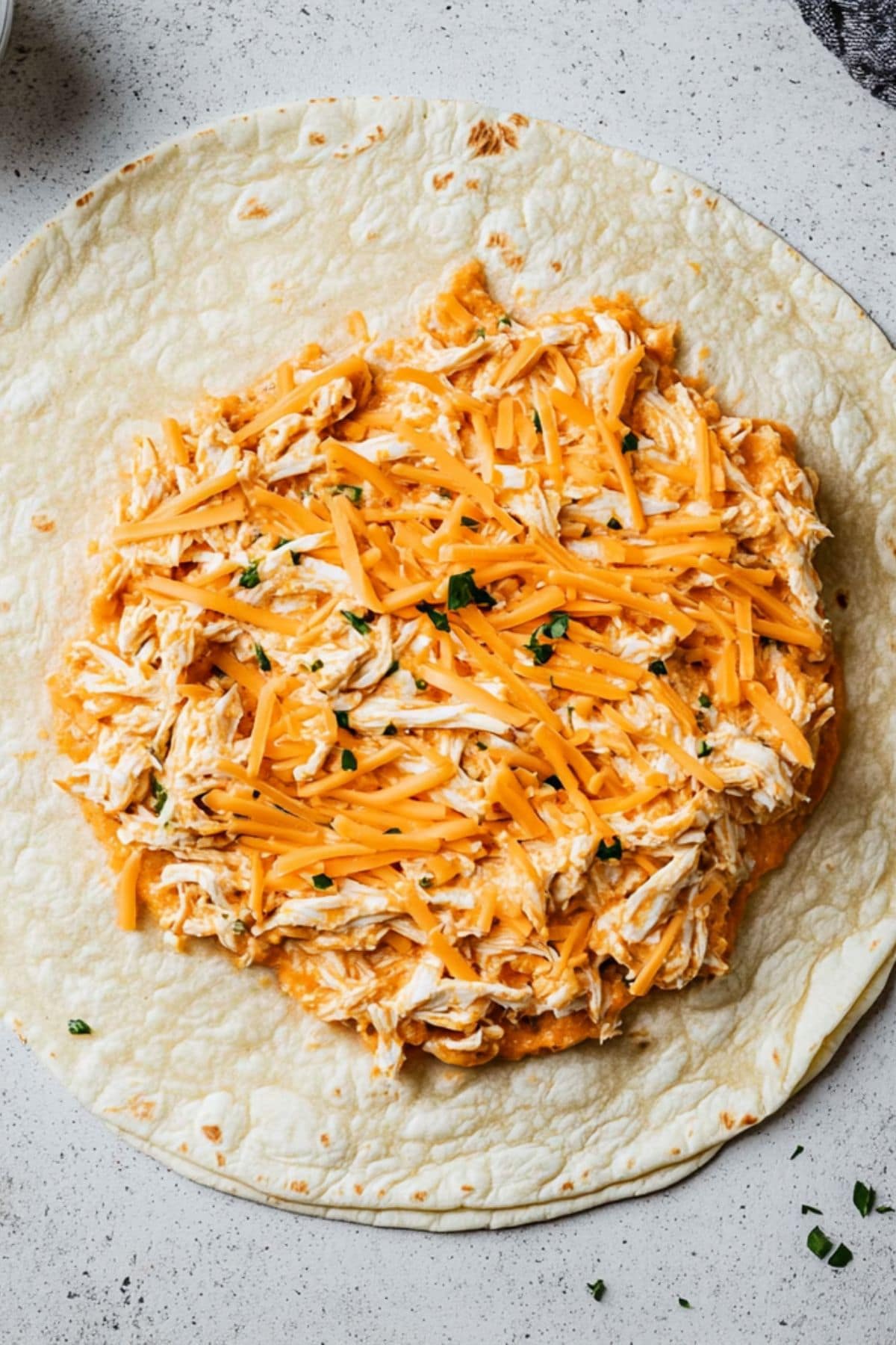 Flour tortilla with shredded buffalo chicken and cheddar cheese, top view.