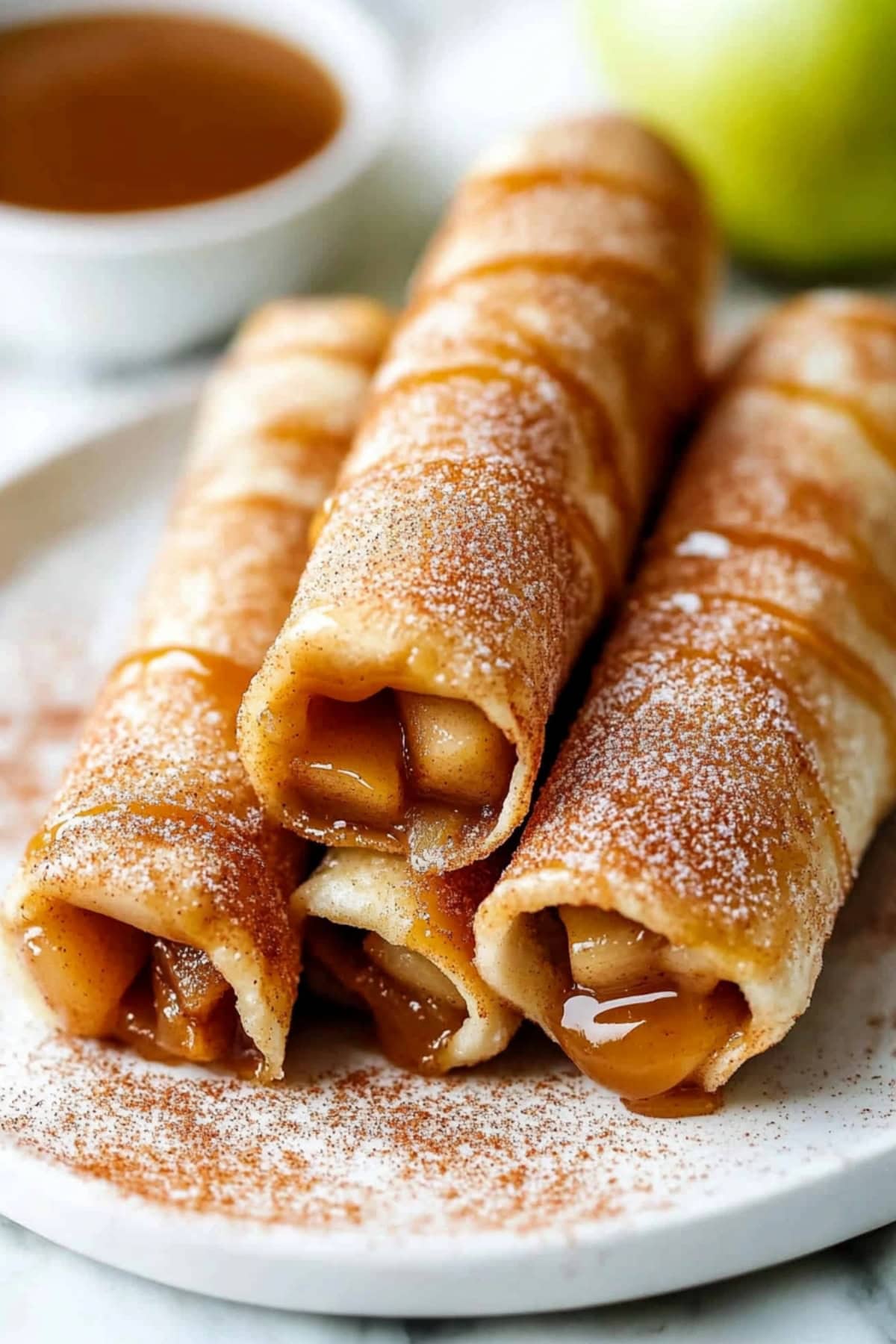 Caramel apple taquitos coated in cinnamon sugar in a white plate.