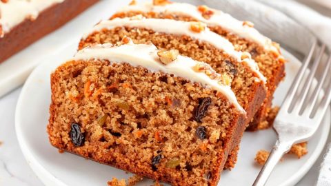 Sliced carrot cake with cream cheese frosting served in a white plate with fork.